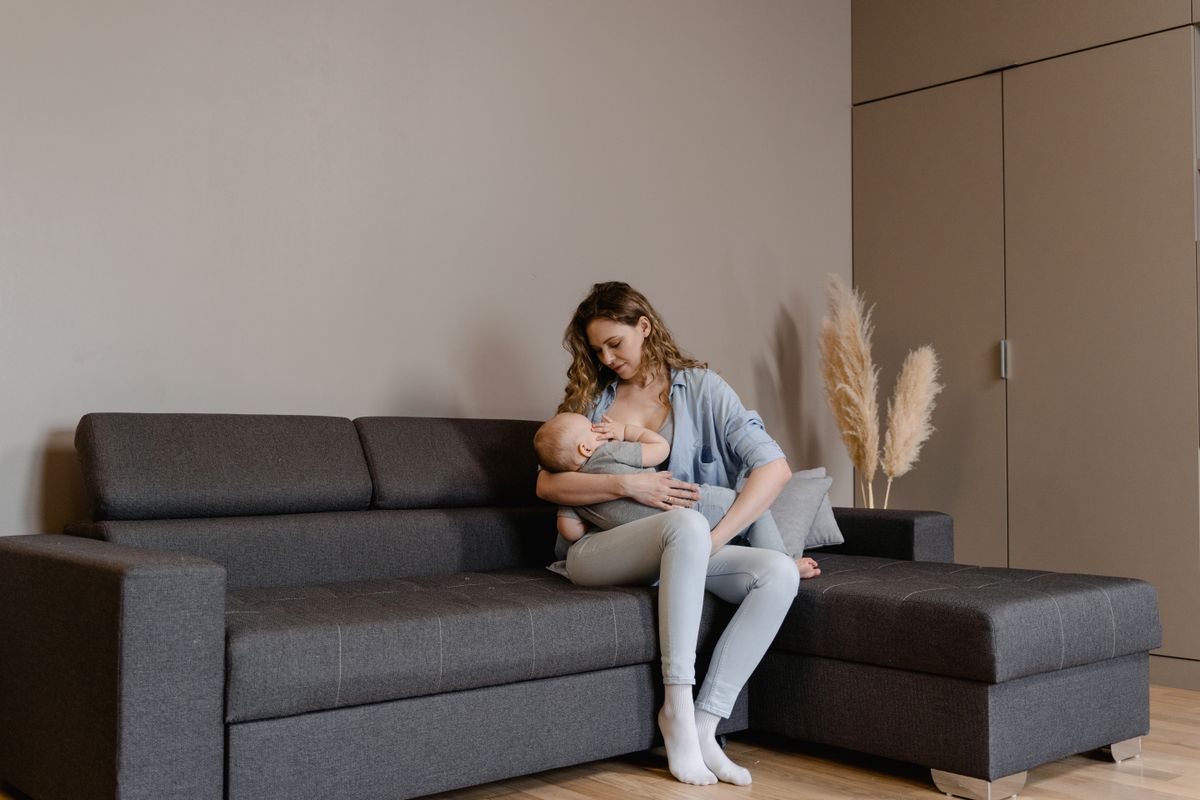 Engravidar amamentando: mãe amamentando bebê no sofá, vínculo maternal e fertilidade no pós-parto